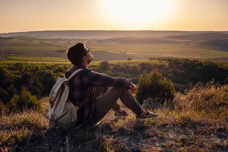 Hiker with backpack sitting on top of the mountain. Orange daybreak at horizon. Lifestyle hiking concept, summer vacations outdoorの写真素材