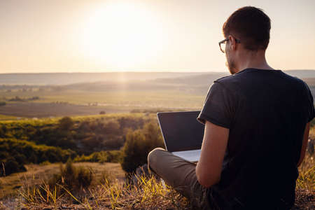 man with laptop sitting on the edge of a mountain with stunning views of the valley. Cellular network broaband coverage concept. 5G.の写真素材