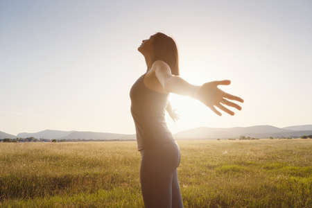 Young girl spreading hands with joy and inspiration facing the sun. She is enjoying serene nature workout vacation outdoors. asian beauty.の写真素材