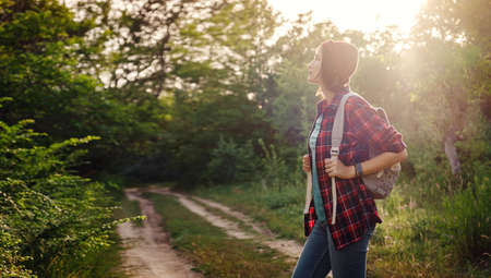 Young hipster girl enjoy sunset at forest. Travel woman with backpack. Enjoying nature sunset. Relaxing in park at sunrise. Trekking conceptの写真素材