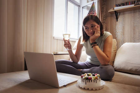 Girl celebrating birthday online in quarantine time. Woman celebrating her birthday through video call virtual party with friends. Authentic decorated home workplace. Coronavirus outbreak 2020.の写真素材
