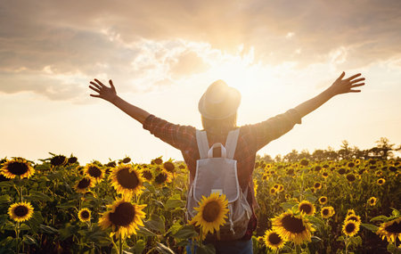 Beautiful young girl enjoying nature on the field of sunflowers. stands back and looks at the...