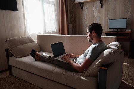 Remote Job. Man Working On Laptop Sitting On Sofa At Home. Copy Space For Text. freelancer hipster...