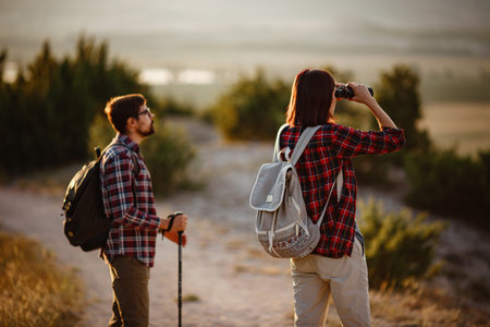 Portrait of happy young couple having fun on their hiking trip. Caucasian and asian hiker couple enjoying themselves on summer vacation. They are watching nature with binoculars.の写真素材