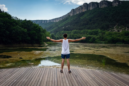 The young male hipster looking at the beautiful view at the lake. Beautiful freedom moment and peaceful atmosphere in nature. Back view.の写真素材