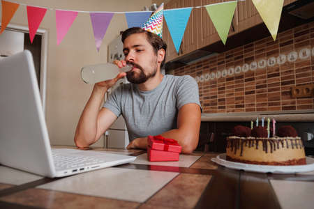 Man celebrating birthday online in quarantine time. Guy celebrating his birthday through video call virtual party with friends. Coronavirus outbreak 2020.の写真素材