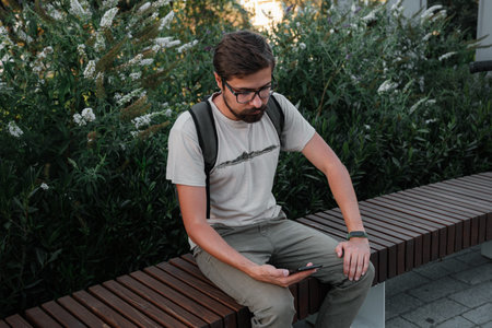 hipster man commuter with electric scooter outdoors in city, using smartphone. Young millennial guy...