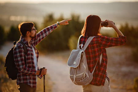 Portrait of happy young couple having fun on their hiking trip. Caucasian and asian hiker couple enjoying themselves on summer vacation. They are watching nature with binoculars.の写真素材