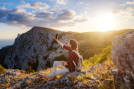 woman hiker enjoy the view at mountain peak cliff, takes pictures on your smartphone or uses apps to communicate..idea of ecotourism travel. Discovery Travel Destination Conceptの写真素材
