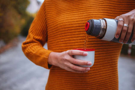 A young tourist woman drinks a hot drink from a cup and enjoys the scenery in the mountains. Trekking concept, Warm autumn weather, calm scene. Wanderlust photo series.の写真素材
