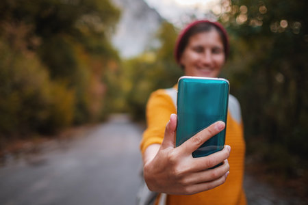 Hipster woman with backpack hold on smart phone gadget in forest. Traveler using mobile on...