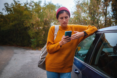 Woman beside a car and looking at smart phone surrounded autumn forest in mountains. Portrait of...