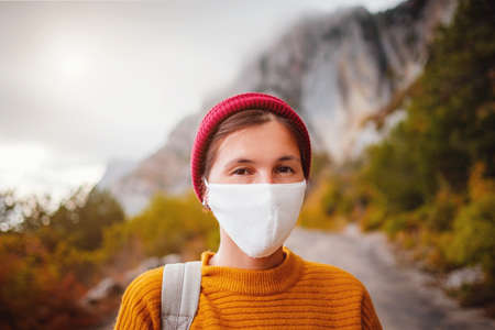 A young woman with a protective face mask is on a walk in nature and she is thinking about when the quarantine ends - topic of corona virus - COVID 19. Wanderlust photo series.の写真素材