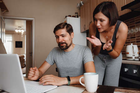 Young couple using laptop and smartphone in the kitchen, smiling man working online at home, family morning lifestyle with gadgets or devices addiction concept. readings newsの写真素材