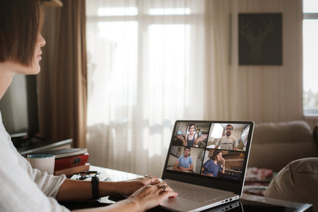 Smiling young asian woman video calling on laptop. Back view photo student looking at computer screen watching webinar or doing video chat by webcam. Over shoulder close up mock up screen view.の写真素材