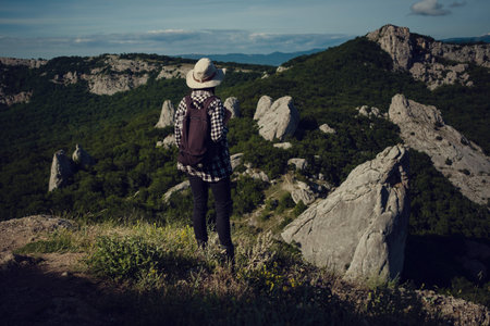 woman traveler with backpack holding hat and looking at amazing mountains and forest, wanderlust...