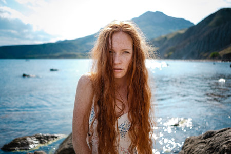 Beautiful boho styled model wearing white dress posing on the beach in sunlight. Red-haired girl with freckles. Crimea, Fox bay, Koktebelの写真素材
