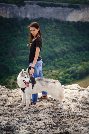 Beautiful girl plays with a dog, gray and white husky, in the mountains at sunset. Indian girl and her wolfの写真素材