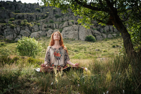 Young girl doing yoga in the park. Calm and meditation. Young red-haired girl under a tree relaxesの写真素材