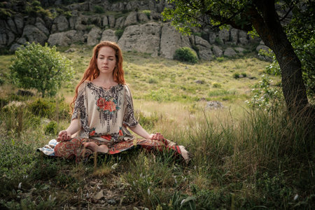 Young girl doing yoga in the park. Calm and meditation. Young red-haired girl under a tree relaxesの写真素材