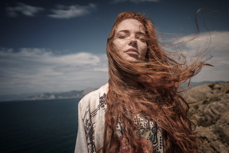 Gorgeous Romantic Girl Outdoors. Beautiful Model near sea. Long Hair Blowing in the Wind. Red-haired girl in ethnic costume on the ocean coastの写真素材