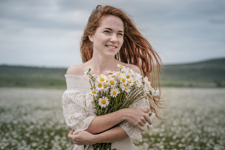 Beautiful young girl with curly red hair in chamomile field. Concept and idea of a healthy...