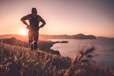 Young standing man with backpack. Hiker on the stone on the seashore at colorful sunset sky. Beautiful landscape with sporty man rocks sea and clouds at sunset. Sporty lifestyleの写真素材