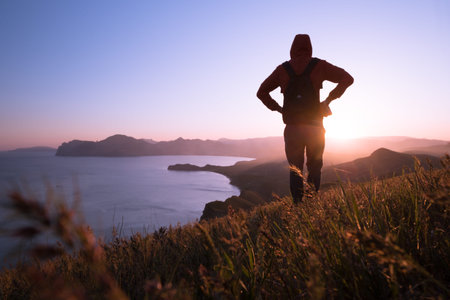 Young standing man with backpack. Hiker on the stone on the seashore at colorful sunset sky....