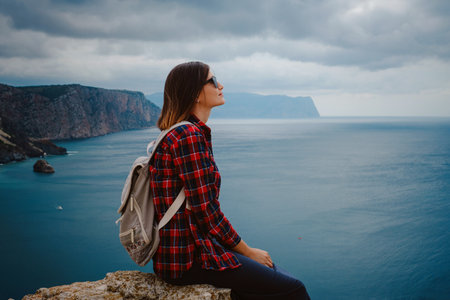 woman traveling with backpack tourist on seashore in summer. Enjoying Beautiful clouds sky among Mighty Cliffs Meeting Ocean. the idea and concept of freedom, vacation and discoveryの写真素材