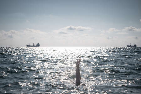 single hand of drowning man in sea asking for help. sticking out of the waterの写真素材