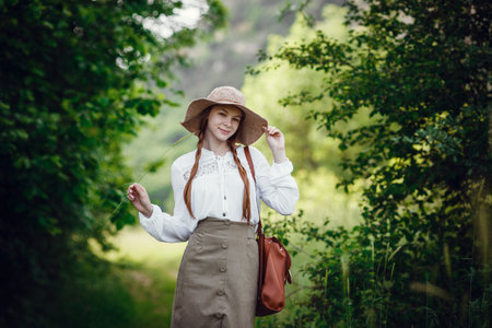 Lovely young woman with red hair, in a hat and with a backpack on the edge of the forest. Beautiful...
