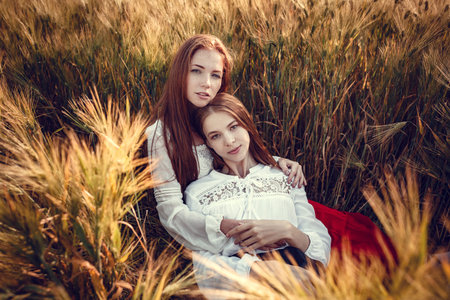 Two young women are looking forward tothe sunset. Best friends. Two young red-haired women in a wheat fieldの写真素材