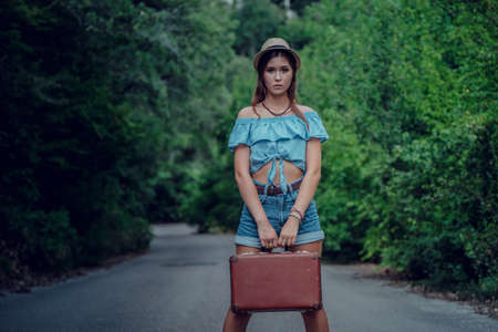 Pretty young woman hitchhiking along a road. Portrait of a beautiful young Asia woman. Image is intentionally toned. Hitchhiking conceptの写真素材