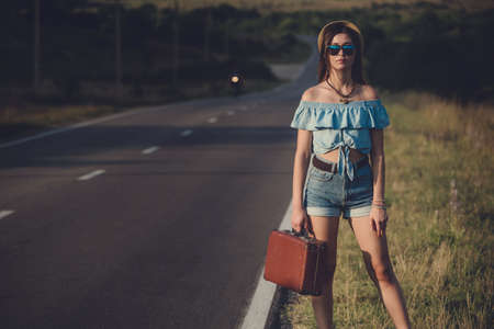 women is hailing a car on a road. Thumbing a ride. Outdoors vacationの写真素材