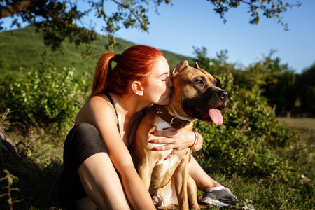redhair jouful young woman caressing their dog, wearing sport clothing, enjoying their time and vacation in sunny parkの写真素材