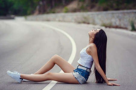 Freedom travel concept. summer weekend. hipster girl wanderlust walking on asphalt road in wild lands. Beautiful young girl with the appearance of southern Asiaの写真素材