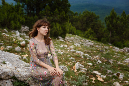 Young happy woman in long dress on the mountainside. Girl on the nature on blue sky background....