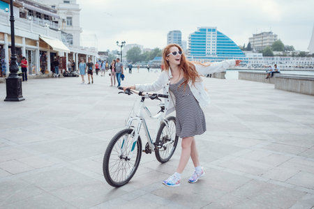 Beautiful woman riding on bike. Lifestyle and health in the city. Cheerful red-haired young woman...