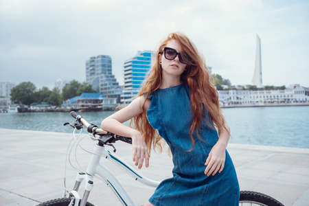 Beautiful woman riding on bike. Lifestyle and health in the city. Cheerful red-haired young woman gets pleasure from walking around the cityの写真素材