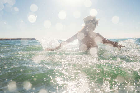Beautiful woman having a fun while swimming in the sea. Beautiful romantic lady in a hat resting at sunsetの写真素材