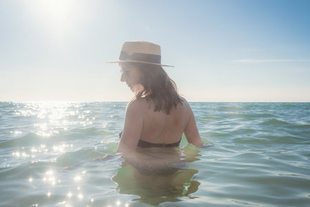 Beautiful woman having a fun while swimming in the sea. Beautiful romantic lady in a hat resting at sunsetの写真素材