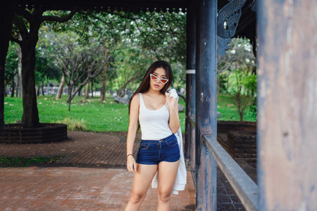 Summer sunny lifestyle portrait of young stylish hipster woman walking on the street, wearing cute trendy outfit. Young Asian women tourist traveler smiling in bangkok. street fashionの写真素材