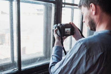 Close-up of hand holding camera. Mirrorless camera close up in the hand of a young man on a studio background. The reporter's taking a picture. the photographer looks into the camera.のeditorial素材