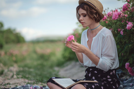 Beautiful young woman with curly hair posing near roses in a garden. The concept of perfume advertisingの写真素材