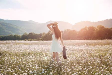 Beautiful girl in daisy field. Summer sunset. happy young lady and spring-green nature, harmony concept. Carefree happy brunette woman with healthy wavy hair having fun outdoor in nature.の写真素材
