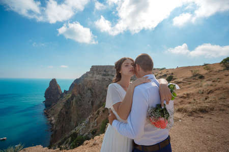Beautiful smiling young bride and groom walking on the beach, kissing and having fun, wedding ceremony near the rocks and sea. Wedding ceremony on coast of Cyprusの写真素材