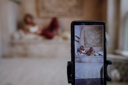Young pretty women takes pictures of himself remotely, using selfie stick, poses in studio. Moroccan...