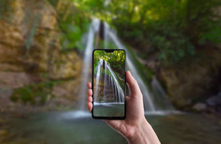A man makes a photo on a smartphone, beautiful landscape of waterfall scenery in the middle of green forest. Beautiful Crimean waterfall Dzhur-dzhurの写真素材