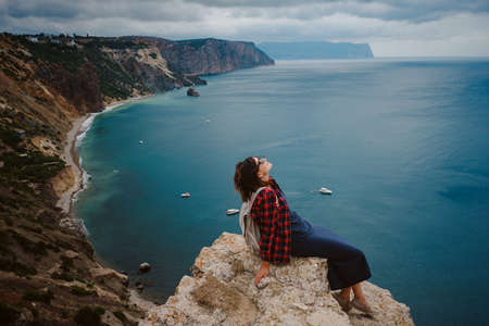 woman traveling with backpack tourist on seashore in summer. Enjoying Beautiful clouds sky among Mighty Cliffs Meeting Ocean. the idea and concept of freedom, vacation and discoveryの写真素材