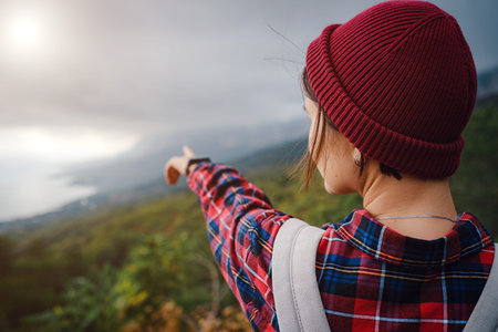 Stylish hipster asian woman with hat walking on top of mountains. Happy young woman with a backpack...